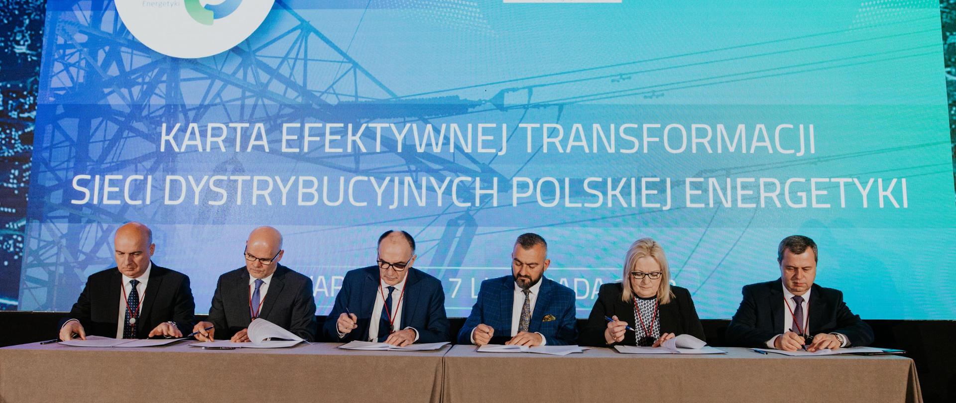 sześć osób za stołem prezydialnym podpisuje dokumenty