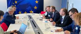 Minister funduszy i polityki regionalnej Grzegorz Puda i komisarz do spraw miejsc pracy i praw socjalnych Nicolas Schmit siedzą na przeciw siebie przy stole obrad, obok nich siedzą pozostali uczestnicy spotkania