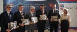 Minister Czarnek, czterech mężczyzn w garniturach i kobieta w białej bluzce stoją w szeregu i trzymają w rękach oprawione w ramki dokumenty.