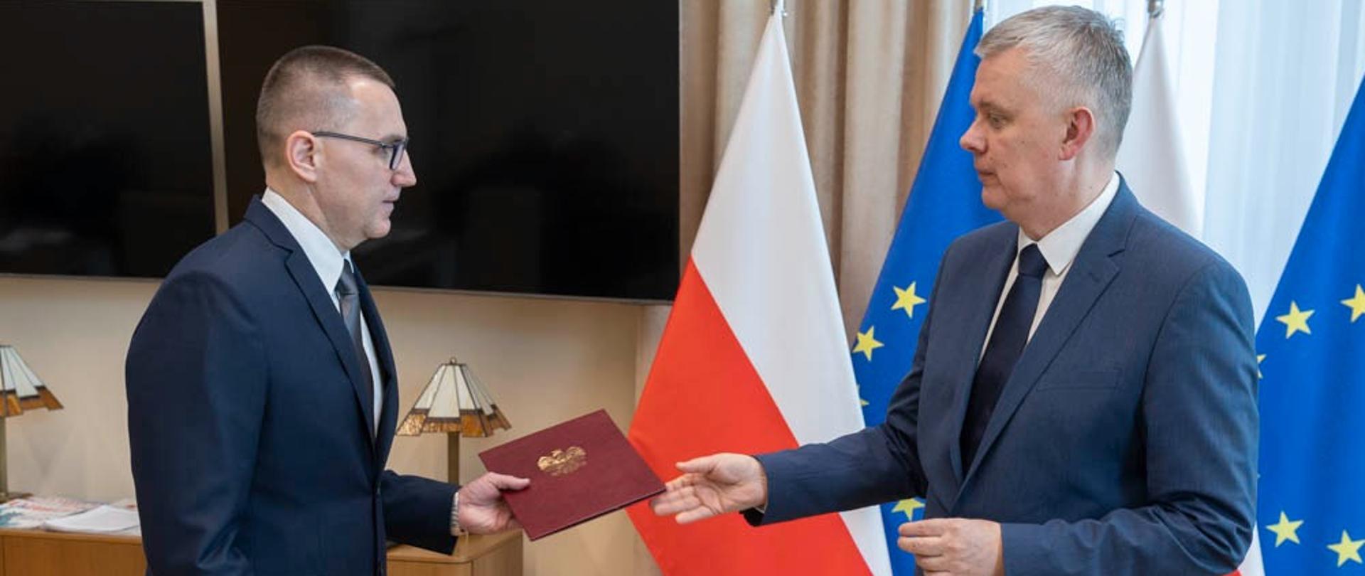 Minister Tomasz Siemoniak wręcza powołanie na tle flag