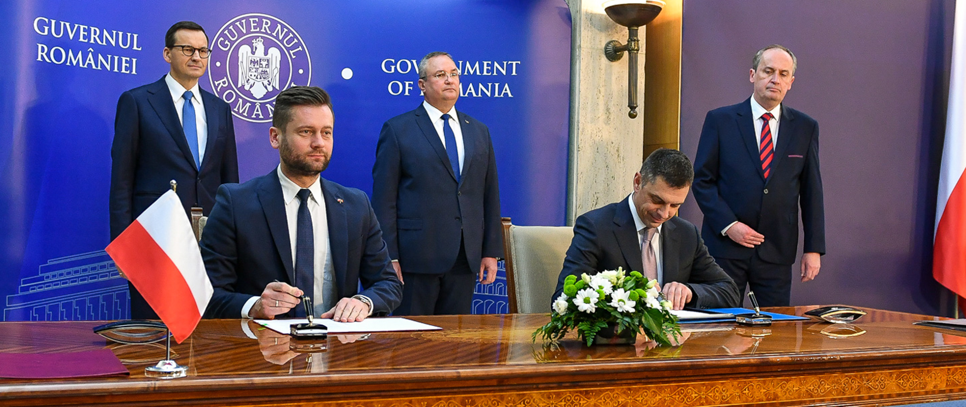 Minister Bortniczuk wziął udział w polsko-rumuńskich konsultacjach międzyrządowych, zdj. MON; ministrowie ds. sportu Polski i Rumunii siedzą przy stole i podpisują memorandum w dziedzinie sportu; za ich plecami stoją premierzy rządów