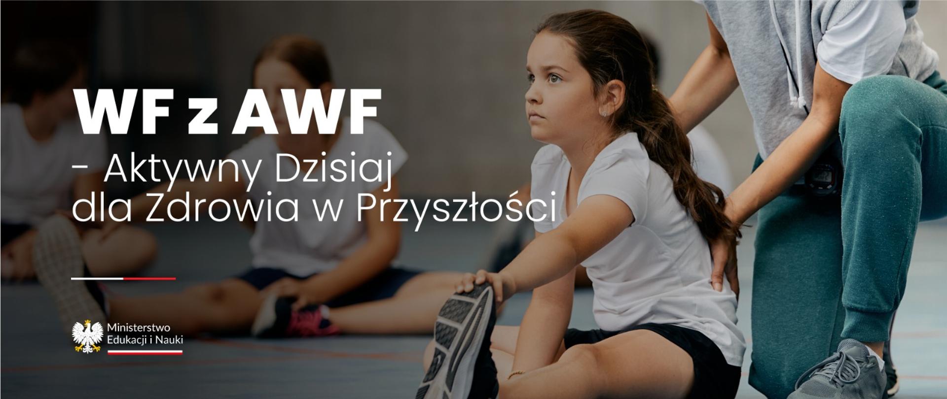 Dziewczynka ubrana w białą koszulke wykonuje skłon w kierunku stopy. Z tyłu kobieta podtrzymuje jej placy. Po lewej stronie napis WF z AWF – Aktywny dzisiaj dla zdrowia w przyszłości 