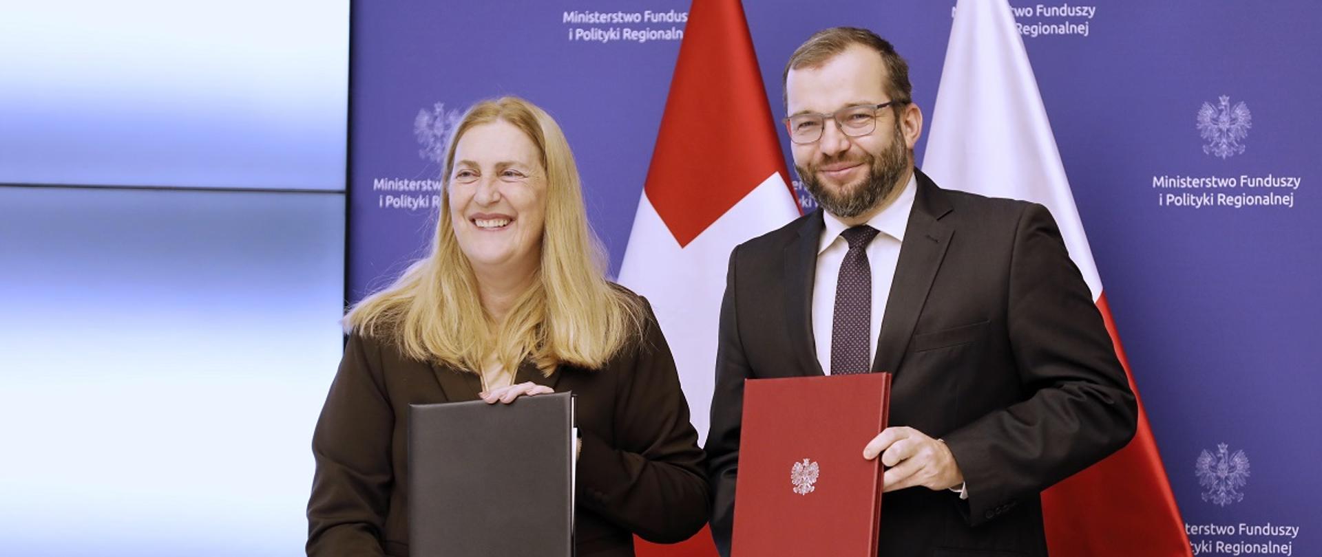 Minister funduszy i polityki regionalnej Grzegorz Puda i sekretarz stanu ds. gospodarki Szwajcarii Helene Budliger Artieda trzymaja w dłoniach umowy na drugą edycję Szwajcarsko-Polskiego Programu Współpracy 