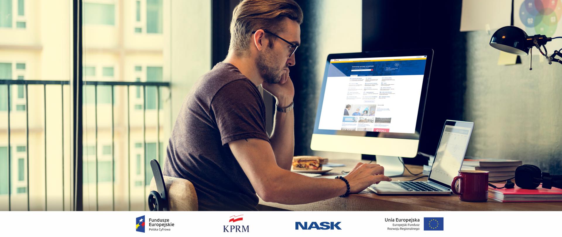 Mężczyzna siedzący przy komputerze, w mieszkaniu, korzysta z laptopa. Obok stoi komputer stacjonarny, na ekranie którego wyświetla się strona główna GOV.pl.