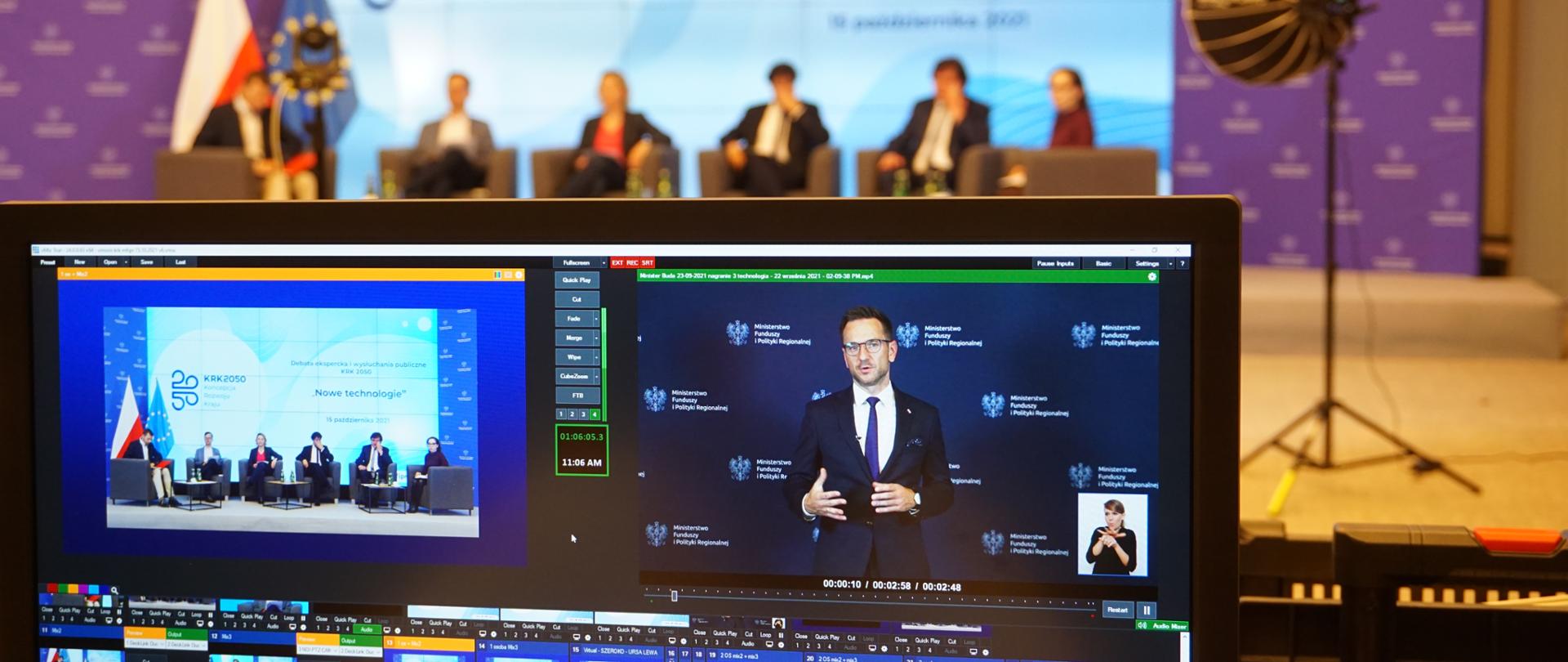 Na pierwszym planie monitor, na którym widać Waldemara Bud. Dalej na fotelach siedzi pięć osób.