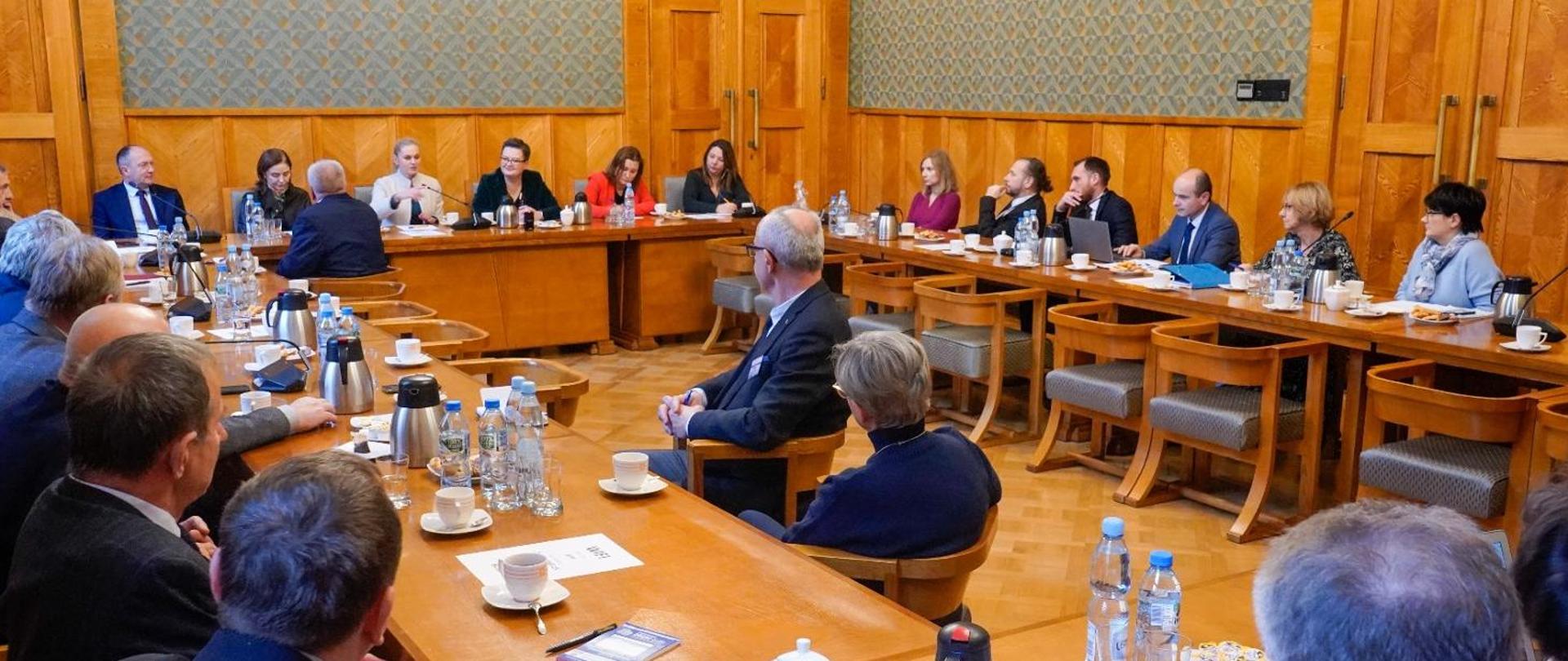 Spotkanie Minister Edukacji Barbary Nowackiej z prezydium Zarządu Głównego ZNP w sali gmachu ministerstwa edukacji. Uczestnicy siedzą w pomieszczeniu, w centrum sali siedzi kierownictwo ministerstwa.