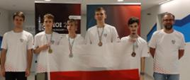 Sześciu młodych ludzi w białych koszulkach stoi przed kolorowym banerem, trzymają polską flagę.