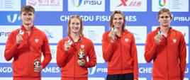 Dwóch mężczyzn i dwie kobiety w czerwonych sportowych bluzach pokazuje trzymane w rękach medale.