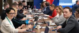 Na zdjęciu widać salę konferencyjną wypełnioną siedzącymi przy stołach uczestnikami spotkania.