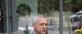 Minister Marek Zagórski przed wejściem do Ministerstwa Cyfryzacji. Przed ministrem widać kilka mikrofonów trzymanych przez dziennikarzy