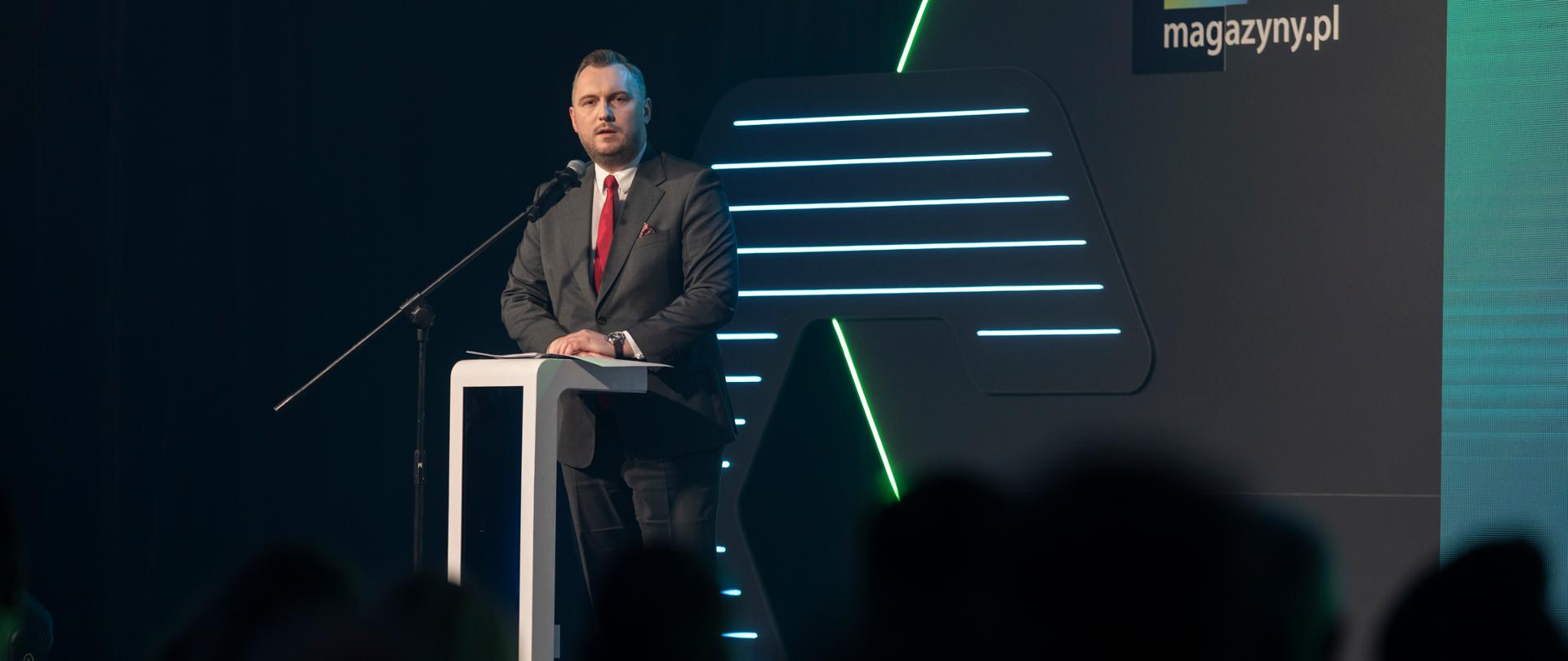 Wiceminister Konrad Wojnarowski na scenie w mównicy z mikrofonem