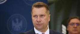 Minister Czarnek stoi przed kilkoma mikrofonami.
