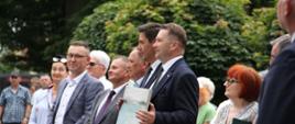 Na dworze stoi duża grupa ludzi,z przodu minister Czarnek trzyma w rękach czworokątny przedmiot.