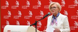 Minister Machałek stoi i mówi do mikrofonu, za nią czerwona ścianka, przed nią mównica z napisem FRSE.