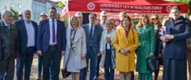 Zdjęcie zbiorowe - minister Czarnek w otoczeniu grupy ludzi stoi przed czerwonym namiotem, w tle miejskie zabudowania.