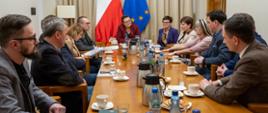 Grupa osób siedzi przy stole. na stole filiżanki, szklanki i butelki z wodą. 