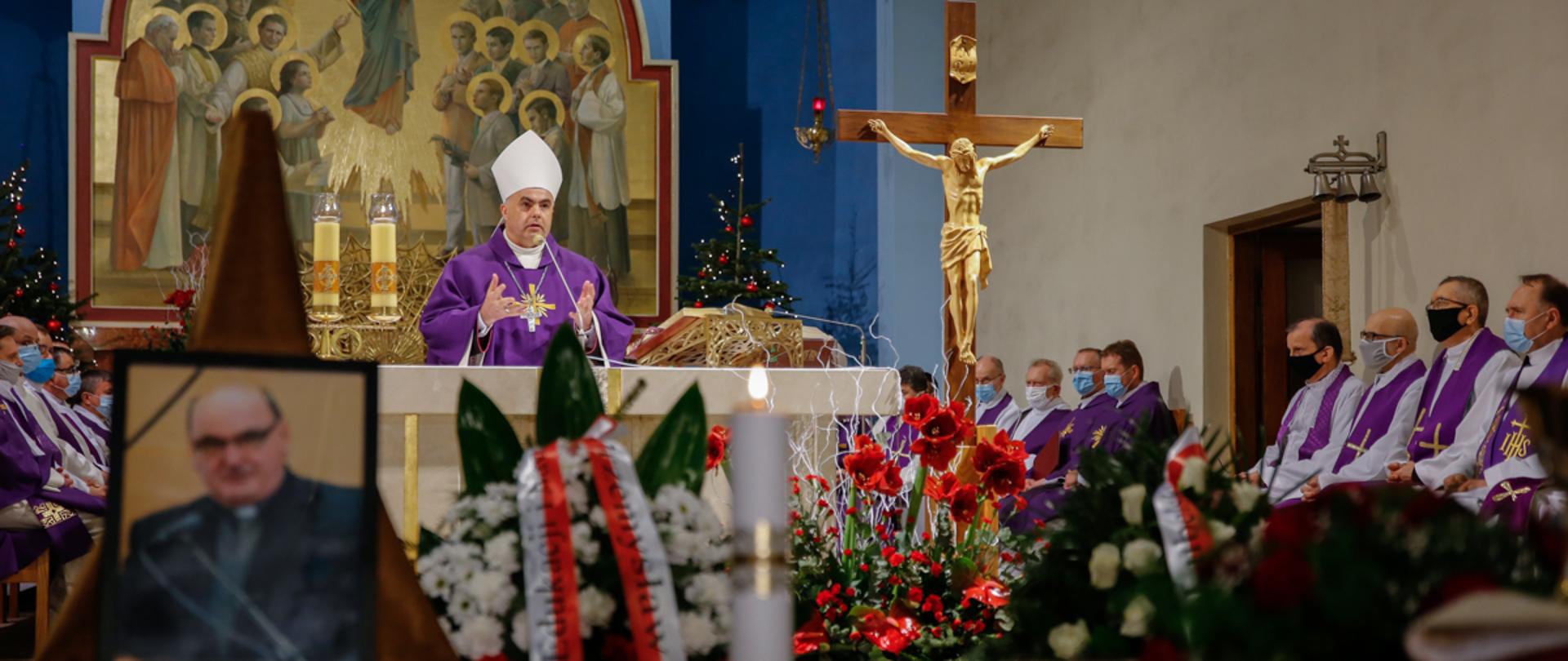 Kościół podczas uroczystości pogrzebowych. W tle biskup w fioletowym ornacie stojący przy ołtarzu. W tle fresk przedstawiający Wniebowzięcie Najświętszej Maryi Panny. Na pierwszym planie fotografia zmarłego księdza Maryniarczyka, winiec z biało-czerwoną szarfą oraz trumna z kwiatami. 