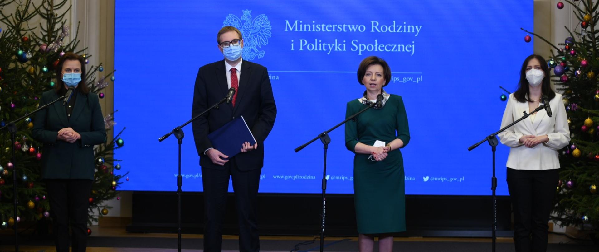 Osoby stoją przed mikrofonami na tle logo Ministerstwa Rodziny i Polityki Społecznej